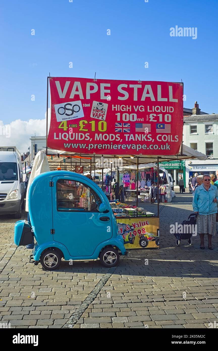Ein türkisfarbener Einsitzer-Mobilitätswagen, der neben einem Vape-Stand auf dem Marktplatz parkt Stockfoto