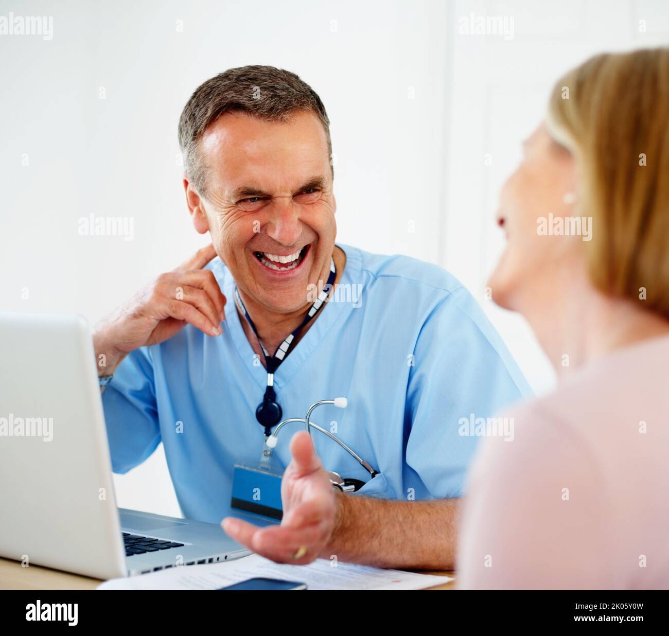 Fröhlicher Arzt im Gespräch mit weiblichen Patienten in der Klinik. Porträt einer fröhlichen Ärztin im Gespräch mit einer Patientin in der Klinik. Stockfoto