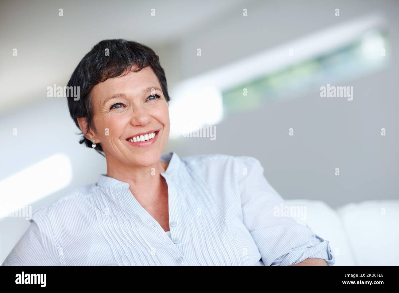 Reife Frau mit selbstbewussten Lächeln. Nahaufnahme einer schönen, reifen Frau, die lächelt, während sie auf der Couch sitzt. Stockfoto