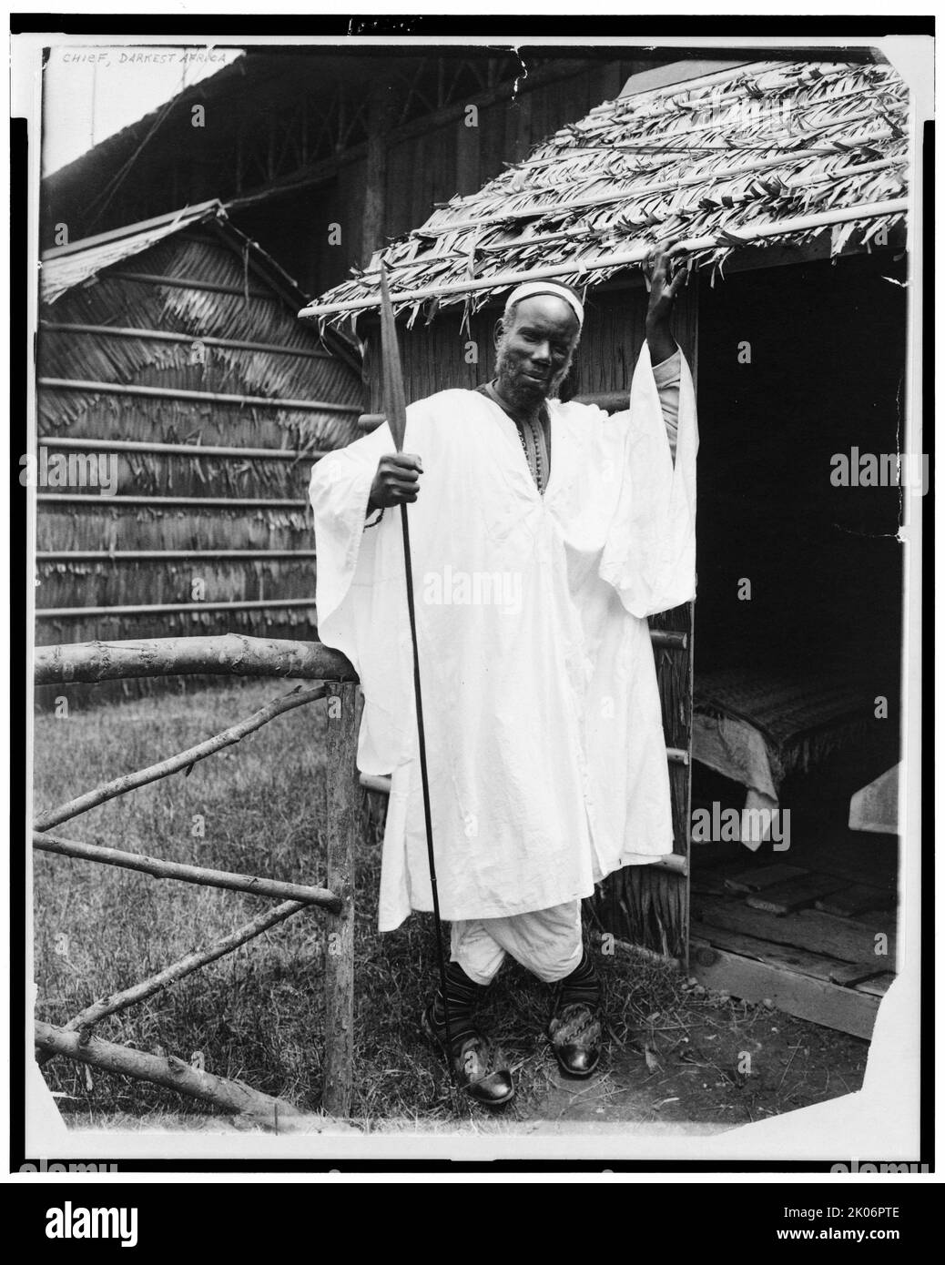 Chef, dunkelstes Afrika, 1901. Afrikanischer Häuptling, in voller Länge, vor der strohgedeckten Hütte stehend, Speer haltend, auf der Panamerikanischen Ausstellung, Buffalo, N.Y. Stockfoto