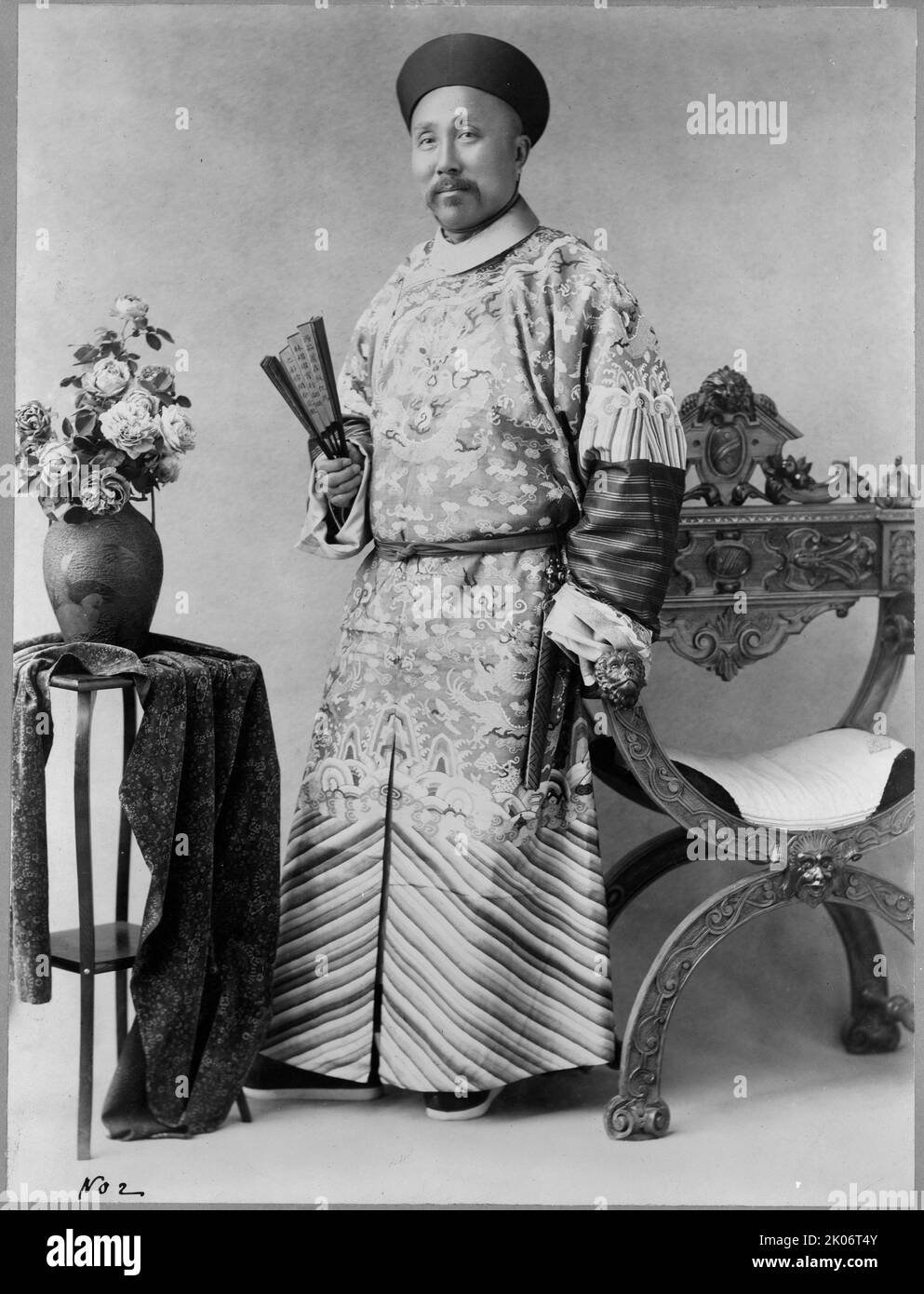 Wu-Ting-Fang, chinesischer Minister, in Washington, D.C., c1900. Dezember 6. Wu Tingfang, chinesischer Diplomat, Porträt in voller Länge, stehend, leicht nach links gerichtet, Einen Ventilator in der rechten Hand halten und die linke Hand auf dem Arm eines Stuhls ruhen; Tisch mit Vase und Blumen auf der linken Seite. Stockfoto