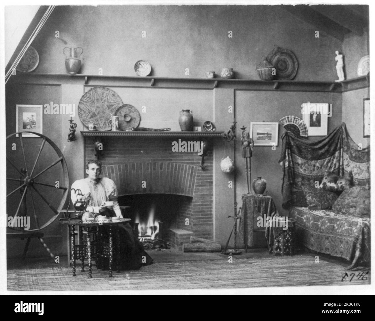 Selbstporträt der Fotografin Frances Benjamin Johnston in ihrem Atelier in der 1332 V Street, N.W., Washington, D.C., c1900. Halblange Ansicht, an einem kleinen Tisch sitzend, etwas nach rechts zeigend; zwischen drehbarem Rad und Kamin. Stockfoto