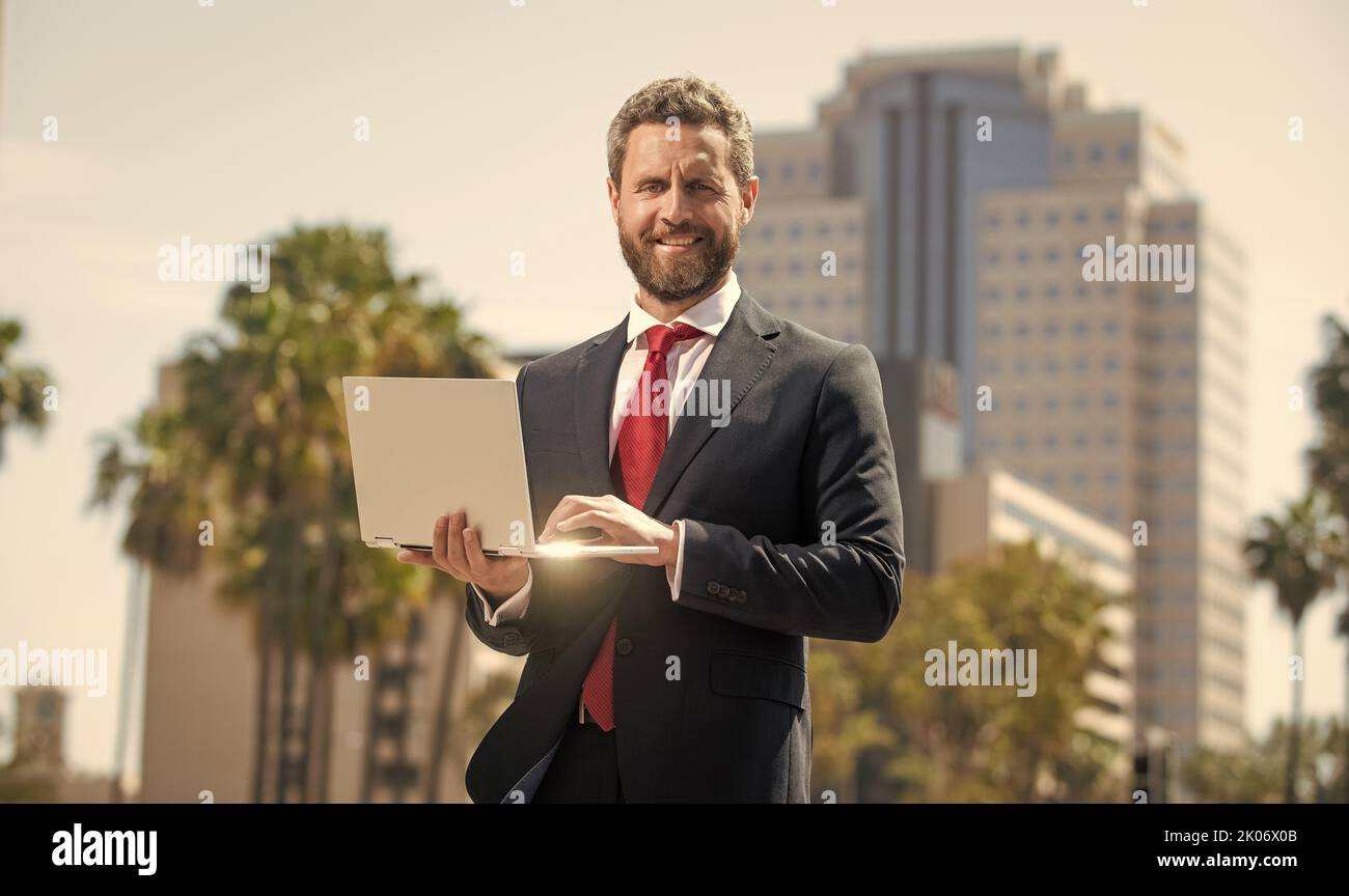 Erfolgreicher glücklicher Geschäftsmann im Anzug, der auf einem Laptop im Freien, im Büro, arbeitet Stockfoto