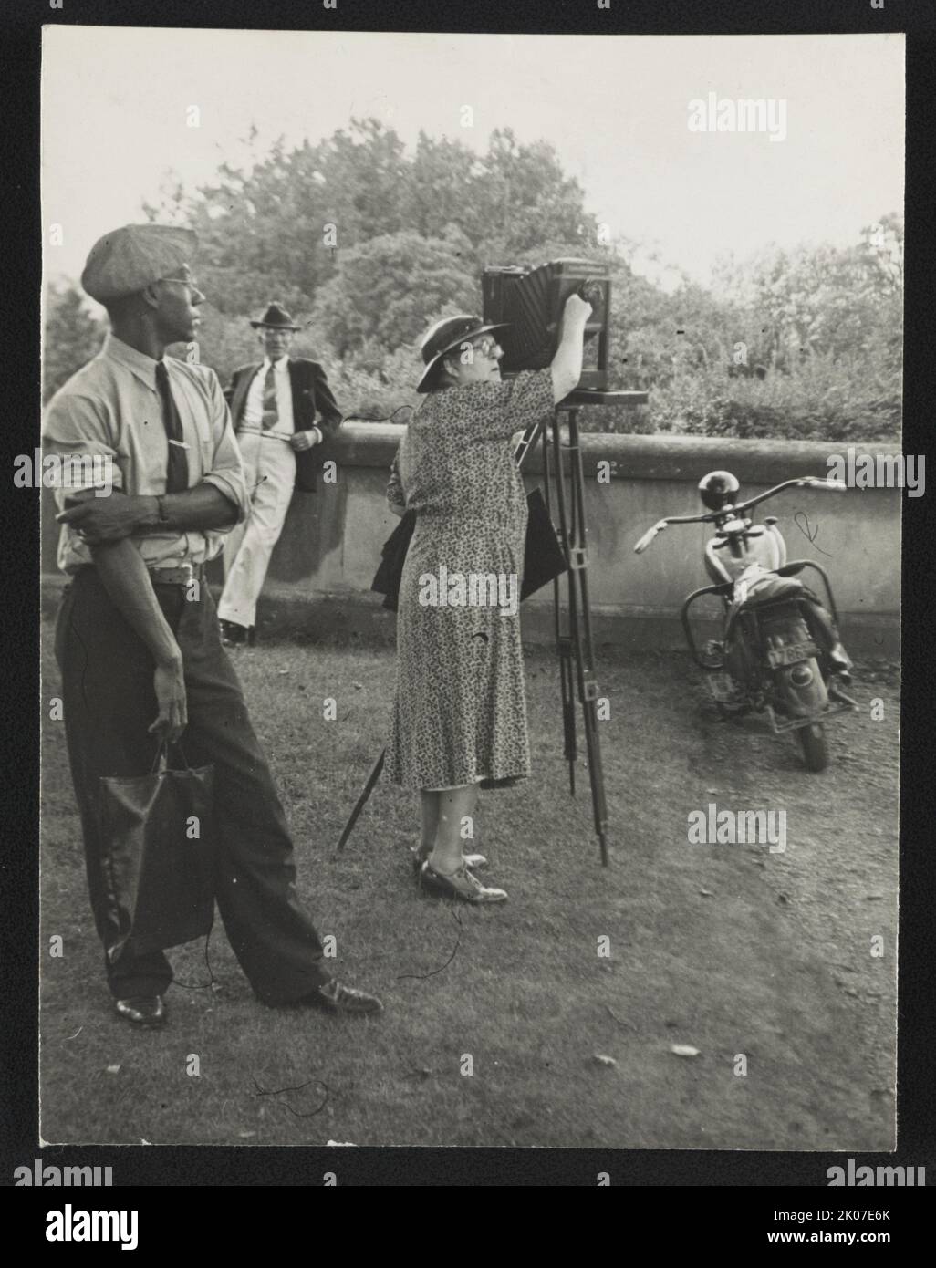 Fotografin Frances Benjamin Johnston steht neben ihrer Sichtkamera und bereitet sich auf ein Foto Biltmore Estate vor; ihre Assistentin Huntley Ruff ist im Vordergrund und ein Motorrad im Hintergrund, 1938. Stockfoto