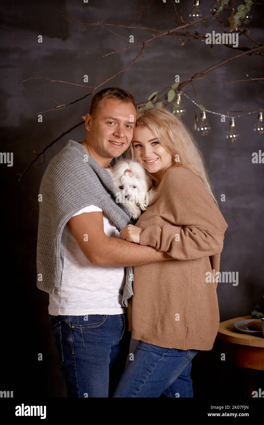 Porträt einer schönen Familie. Romantisches Paar mit ihrem Hund in der Nähe von Weihnachtsbaum in festlichen ästhetischen gemütlichen Wohnräumen. Gute Laune der Weihnachtsliebe Stockfoto