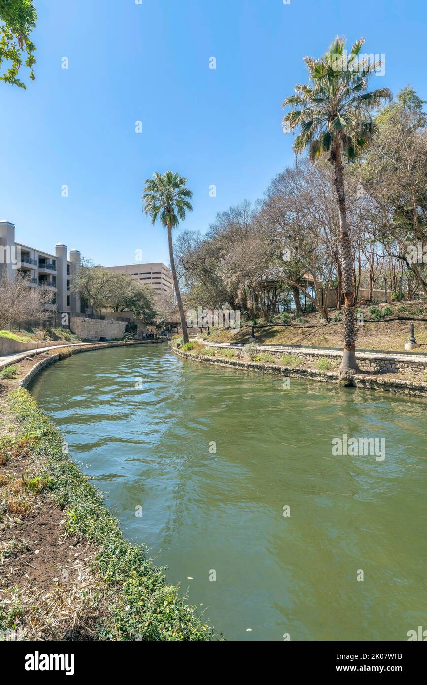 Der River Walk in San Antonio Texas mit einem gewundenen Kanal, der von Wanderwegen flankiert wird. Landschaftlich reizvolle Ausblicke auf die Natur und Gebäude können auf diesem auch gegen den blauen Himmel gesehen werden Stockfoto