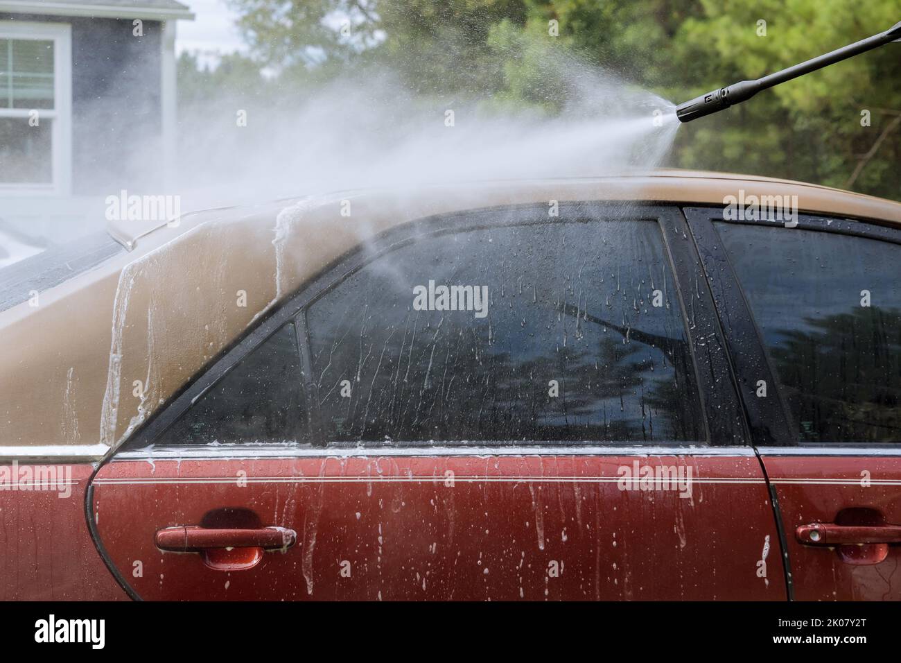 Die zeigt einen Mann, der sein Auto mit dem Hochdruckstrahl wäscht, der Wasser spritzt Stockfoto