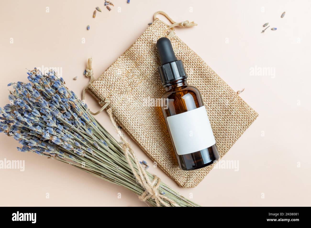 Draufsicht auf dunkle Glasflasche mit Lavendel aromatischem ätherischem Öl oder Extrakt auf beigem Hintergrund. Bund duftender trockener Lavendel-Haufen. Haut A Stockfoto