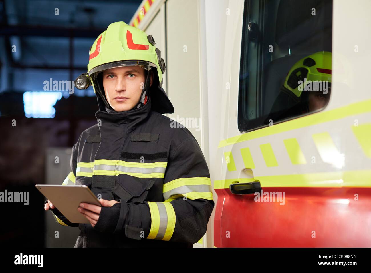 Männlicher Feuerwehrmann mit Tablette in Uniform auf Autohintergrund Stockfoto