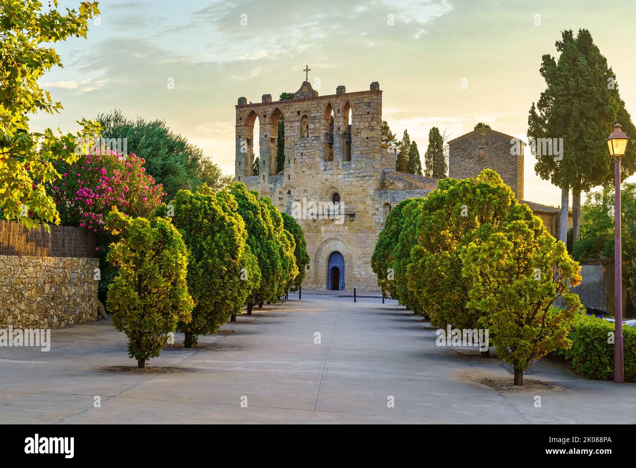 Alte Steinkirche mit Spaziergang mit Bäumen bei Sonnenuntergang in der Stadt Peratallada, Girona, Spanien. Stockfoto