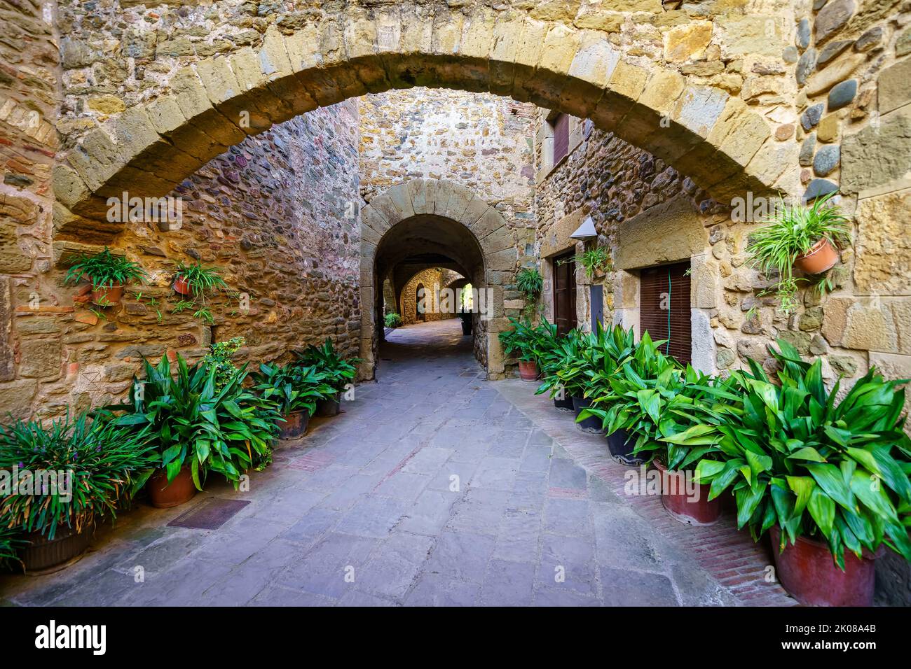 Malerische Gasse mit Steinhäusern und gewölbtem Durchgang mit grünen Pflanzen auf dem Boden, Monells, Girona, Spanien. Stockfoto