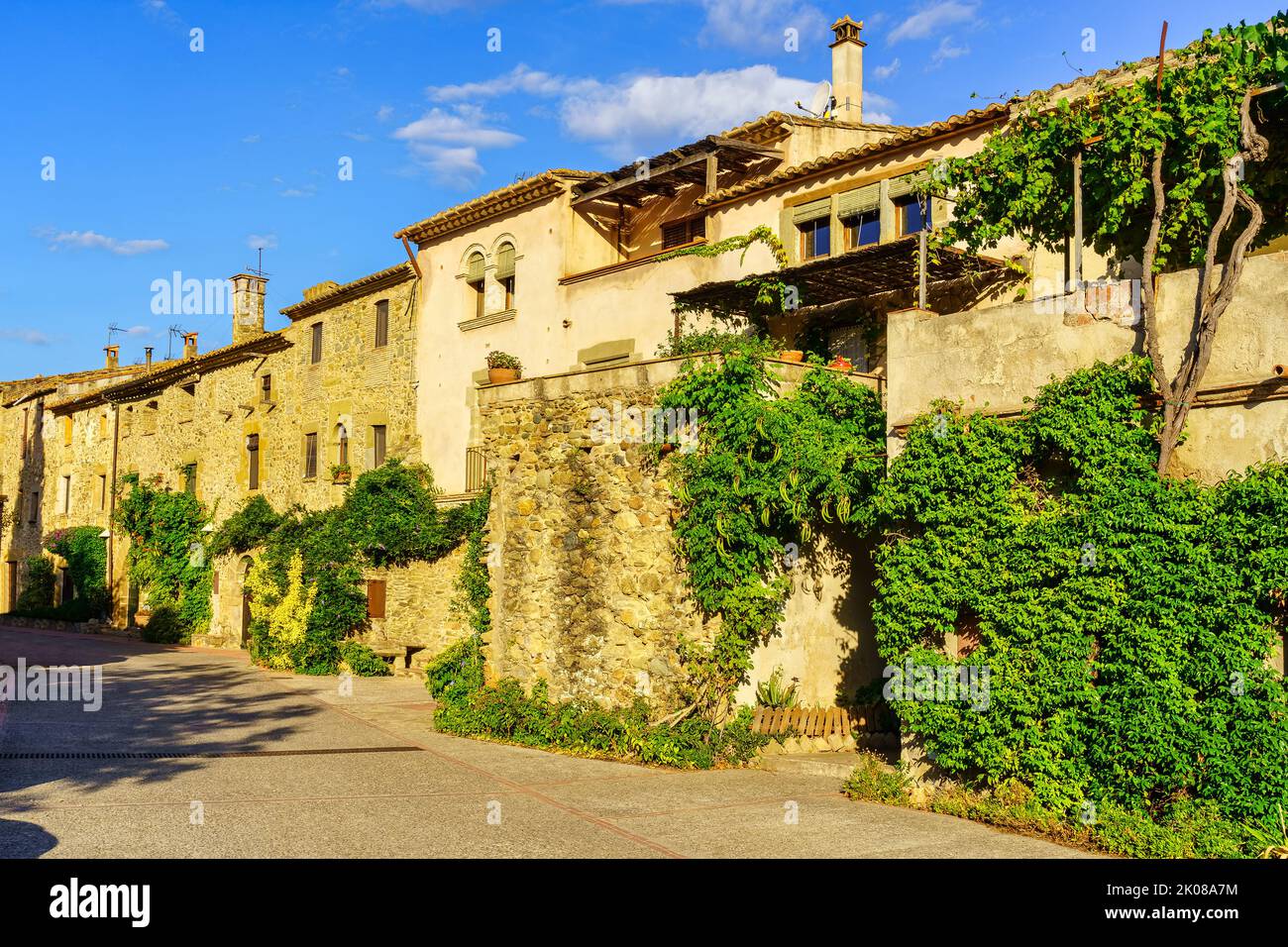 Traditionelle Steinhäuser mit grünen Blumentöpfen und Blumen im katalanischen Dorf Monells, Girona. Stockfoto