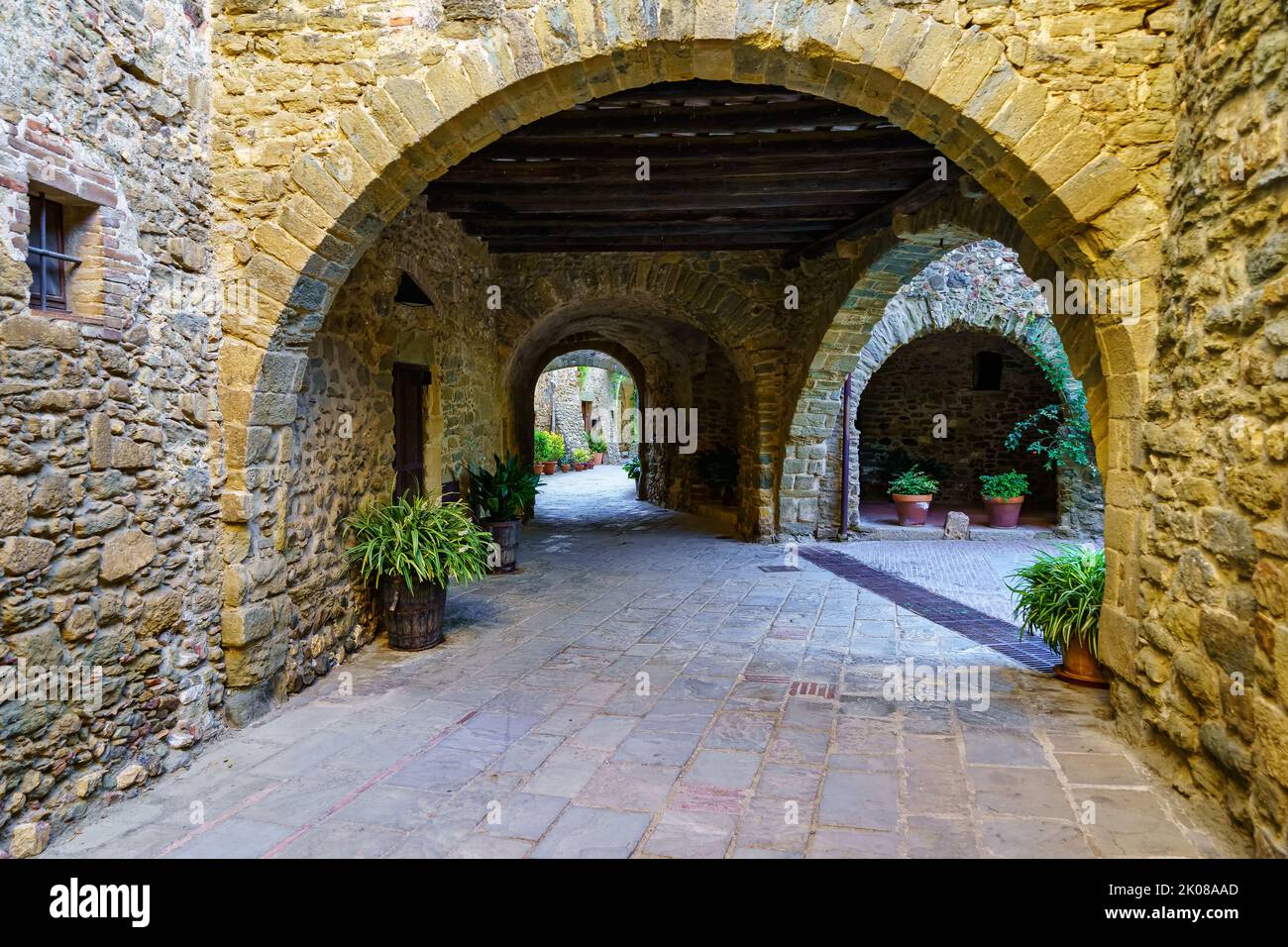 Malerische Gasse mit Steinhäusern und gewölbtem Durchgang mit grünen Pflanzen auf dem Boden, Monells, Girona, Spanien. Stockfoto