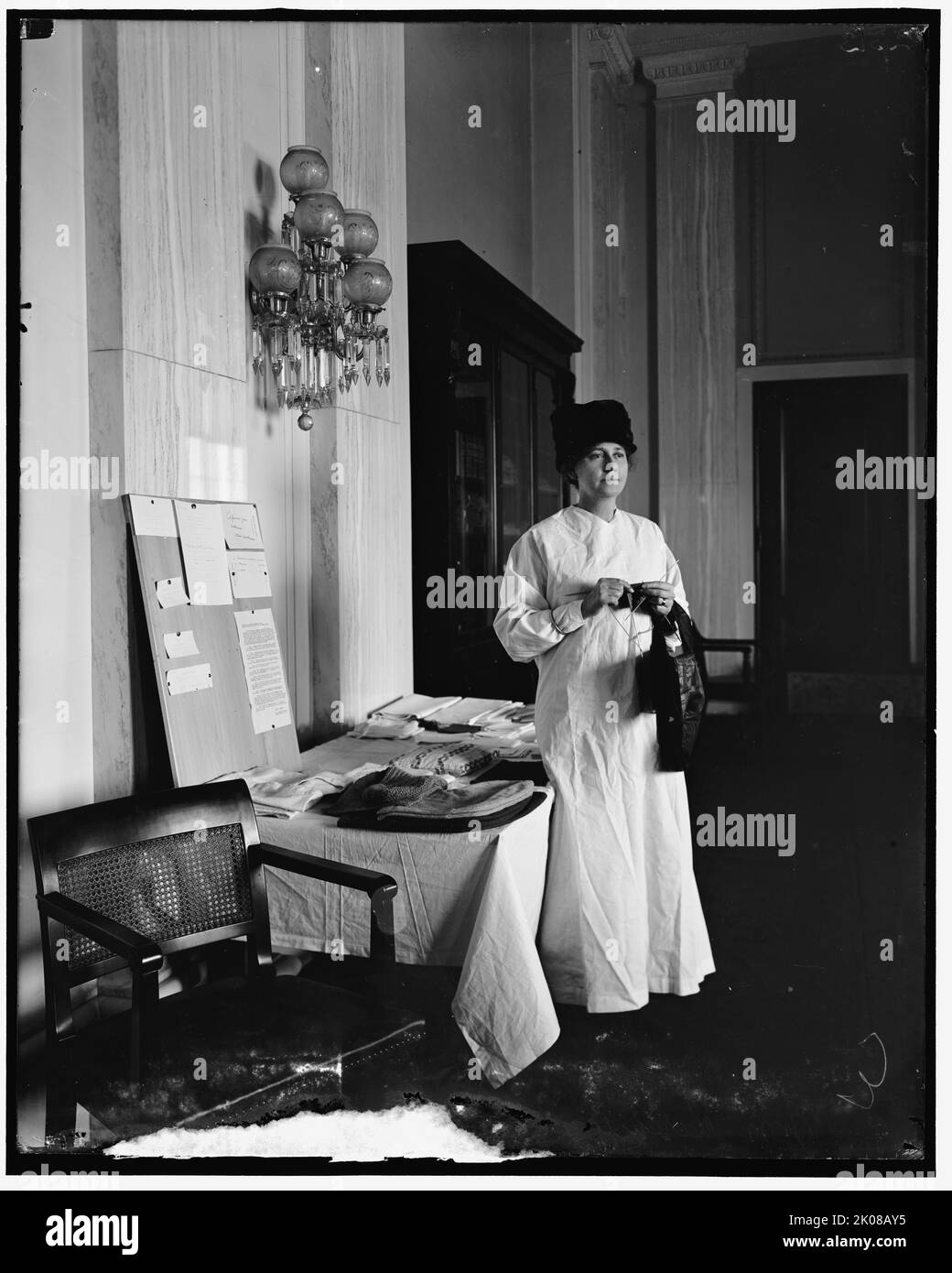Frau Thomas Marshall, zwischen 1910 und 1920. Frau strickt, mit der Anzeige von Schürzen und gestrickten Gegenständen zum Verkauf, möglicherweise eine Spendenaktion. Schild auf US-Senat-Notenpapier geschrieben. Stockfoto