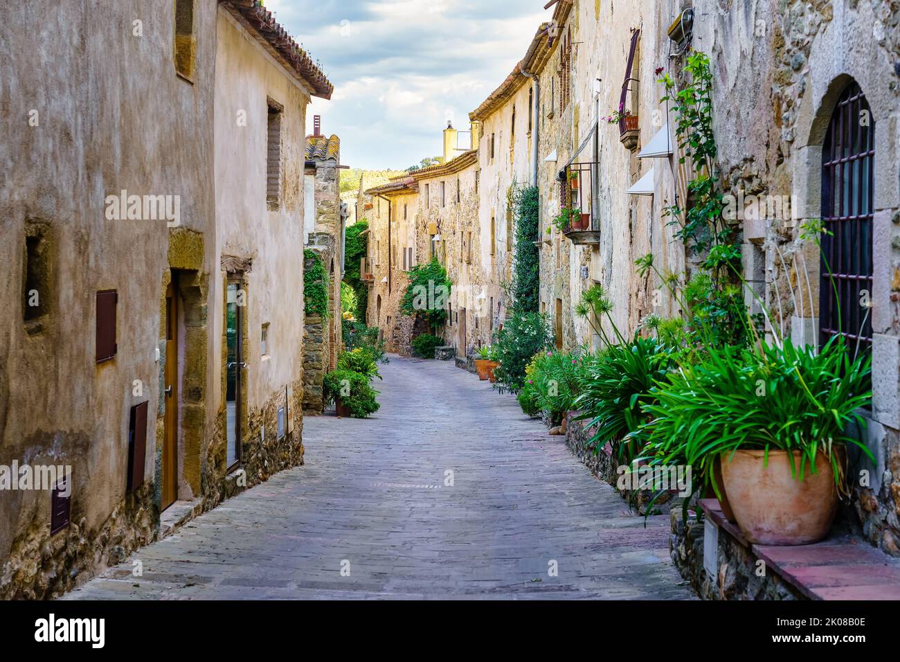 Schöne Gasse mit alten Steinhäusern und Töpfen auf der Straße mit Pflanzen und Blumen, Monells, Girona, Katalonien. Stockfoto