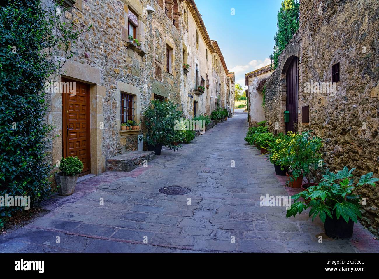 Schöne Gasse mit alten Steinhäusern und Töpfen auf der Straße mit Pflanzen und Blumen, Monells, Girona, Katalonien. Stockfoto