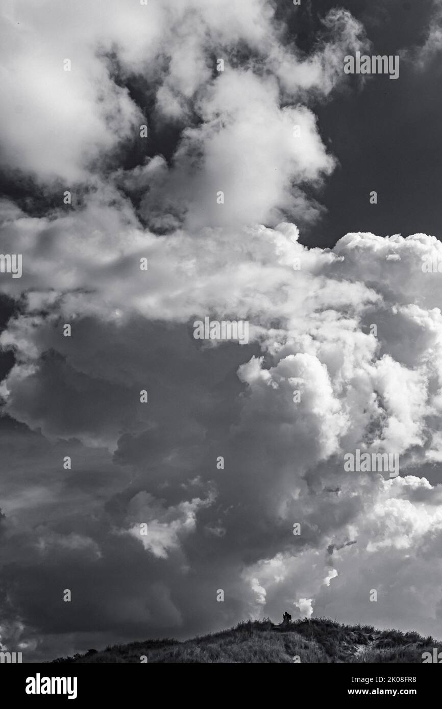 Schwarzweiß-Hochformat-Bild eines Landschaftsfotografen, der winzig unter einer riesigen, hoch aufragenden Kumuluswolke aussieht Stockfoto