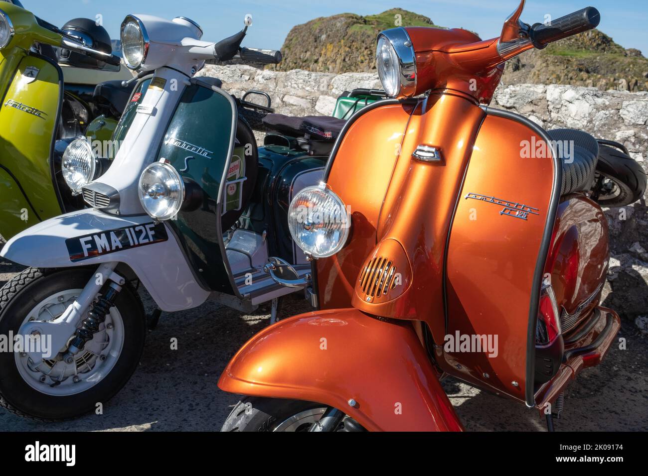 Drei klassische italienische Lambretta-Motorroller entlang der Meeresmauer am Hafen, Treffen der Clans-Rallye. Ballintoy, Großbritannien - 10. September 2022. Stockfoto
