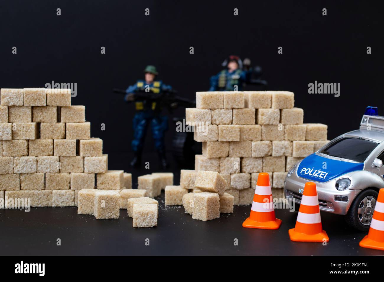 Polizei-Spielzeug bricht eine Zuckerwürfel Wand, auf schwarzem Hintergrund, Diät Polizei kreative Konzept, aus nächster Nähe. Stockfoto