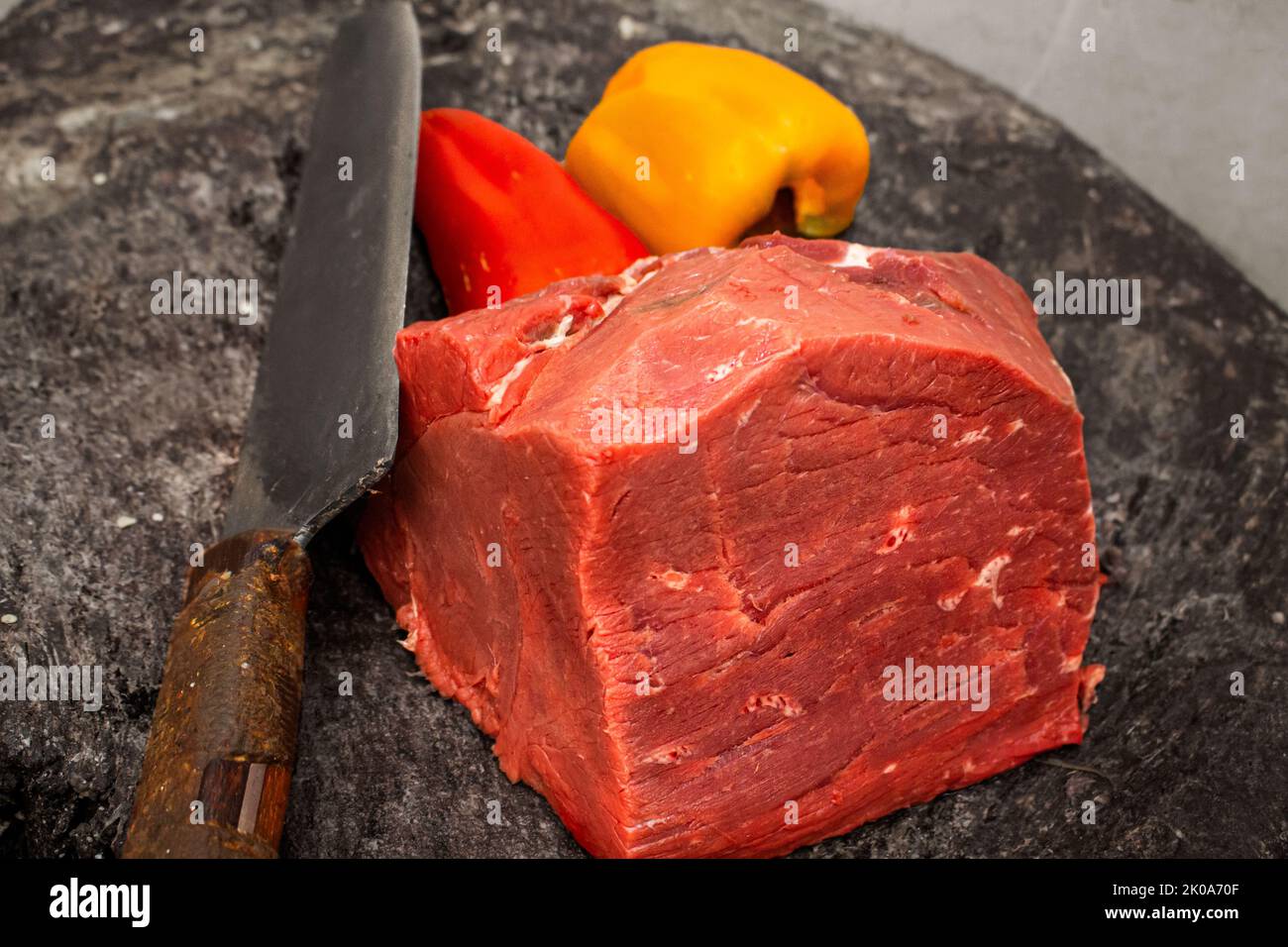 Frisches rohes Rindfleisch mit Messer und lebendiger Paprika auf rustikaler Oberfläche Stockfoto