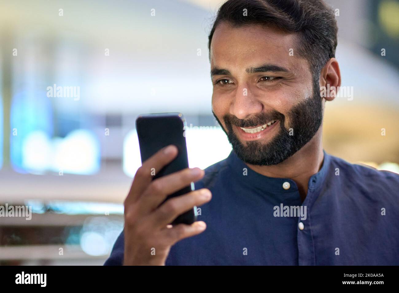 Lächelnder indischer Geschäftsmann mit Smartphone und Blick auf Handy. Stockfoto