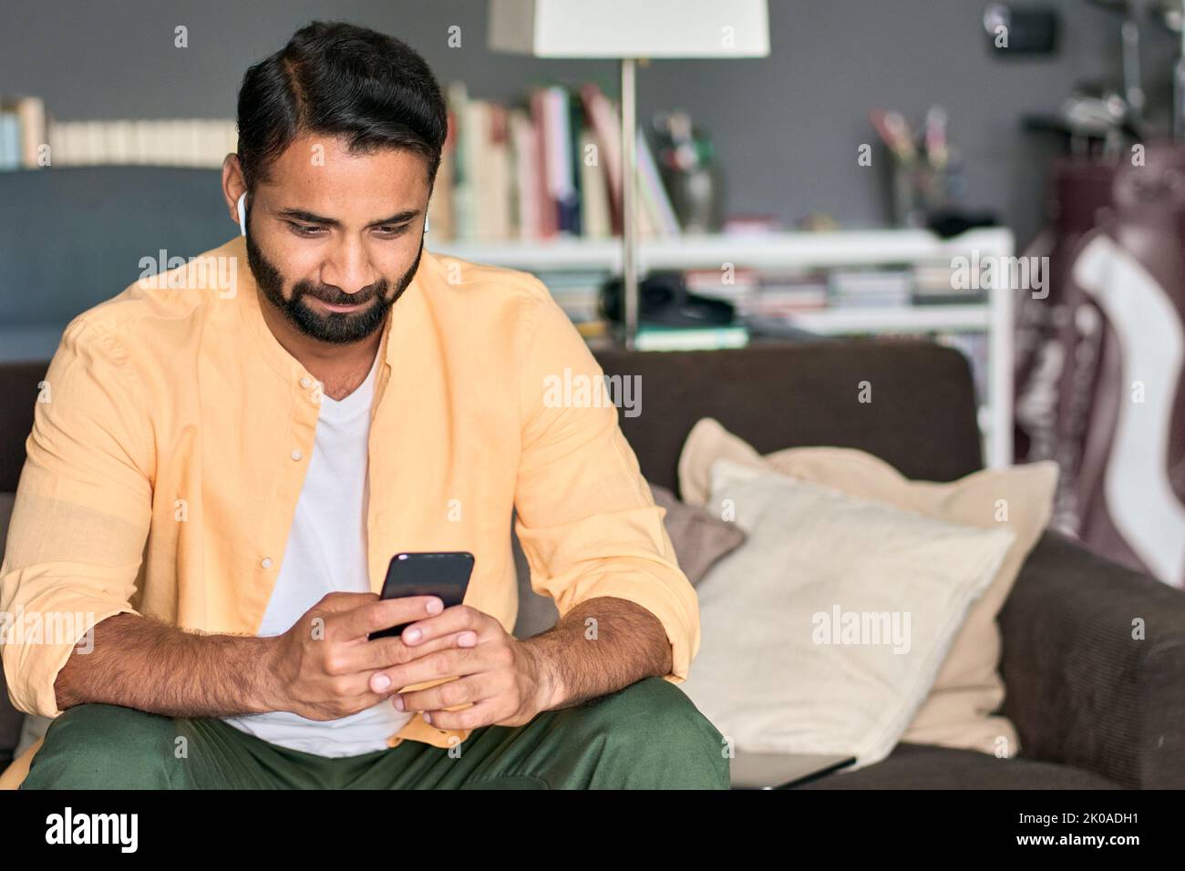 Indischer Mann, der zu Hause auf der Couch sitzt und Videos mit dem Smartphone ansieht. Stockfoto