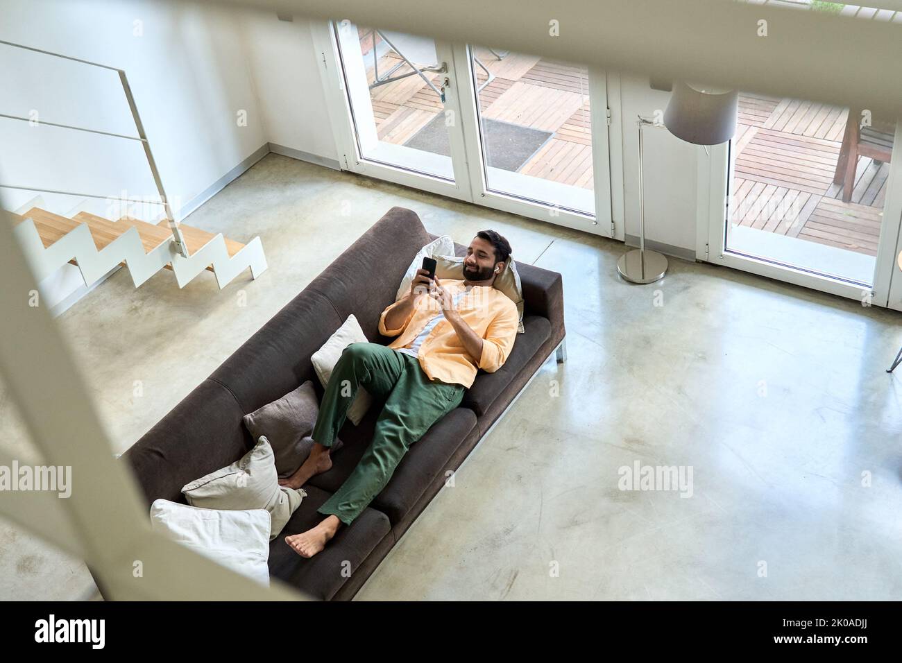 Entspannter indischer Mann, der zu Hause mit dem Handy auf der Couch chillt. Draufsicht Stockfoto