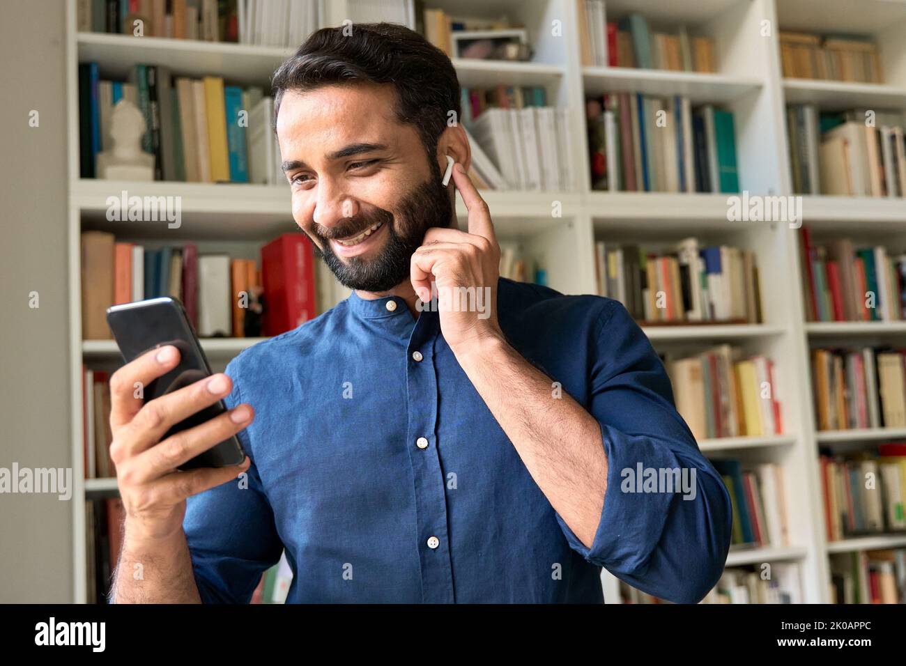 Glücklicher indischer Geschäftsmann mit Ohrstöpsel und Videoanruf über Mobiltelefon. Stockfoto