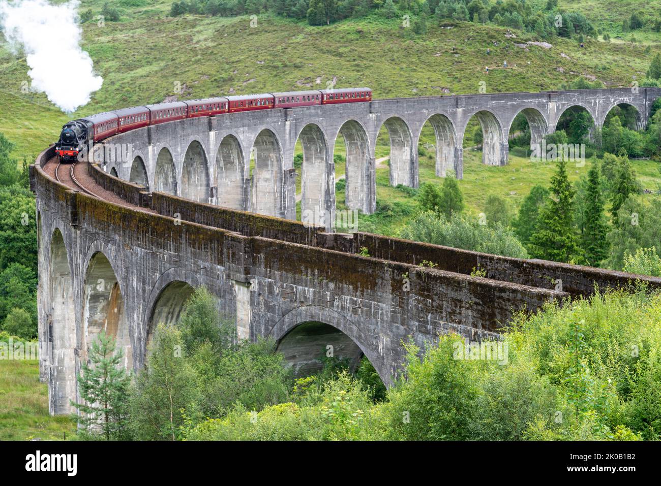Die Jacobite Dampflokomotive und kunstvolle Kutschen, die die ikonische Viaduktbrücke überqueren, auf der West Highland Line, beliebter Touristenort und Wahrzeichen, Stockfoto