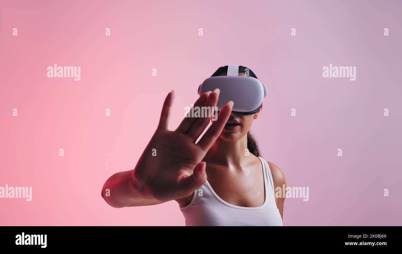 Die Gambin nutzt ihre Hand, um mit dem virtuellen Raum zu interagieren, während sie ein Virtual-Reality-Headset trägt. Junge Frau erlebt eine Simulation von 3D in einem Gestüt Stockfoto