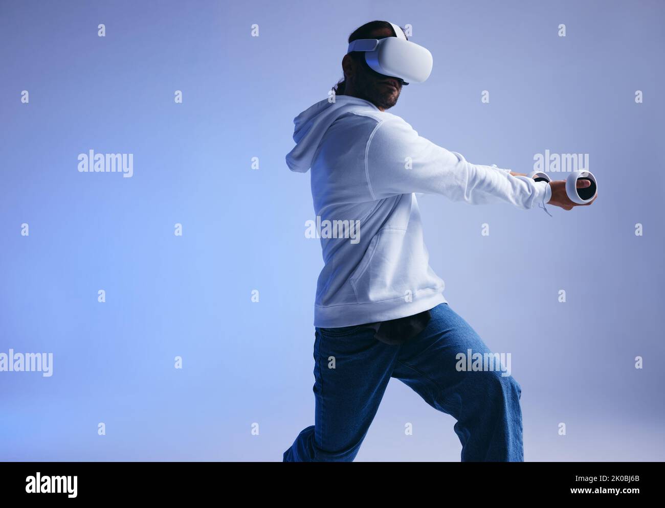 Cricket in der virtuellen Realität. Sportlicher junger Mann, der mit Gaming-Controllern einen virtuellen Ball schlägt. Aktiver junger Mann, der beim Tragen immersive VR-Spiele erforscht Stockfoto
