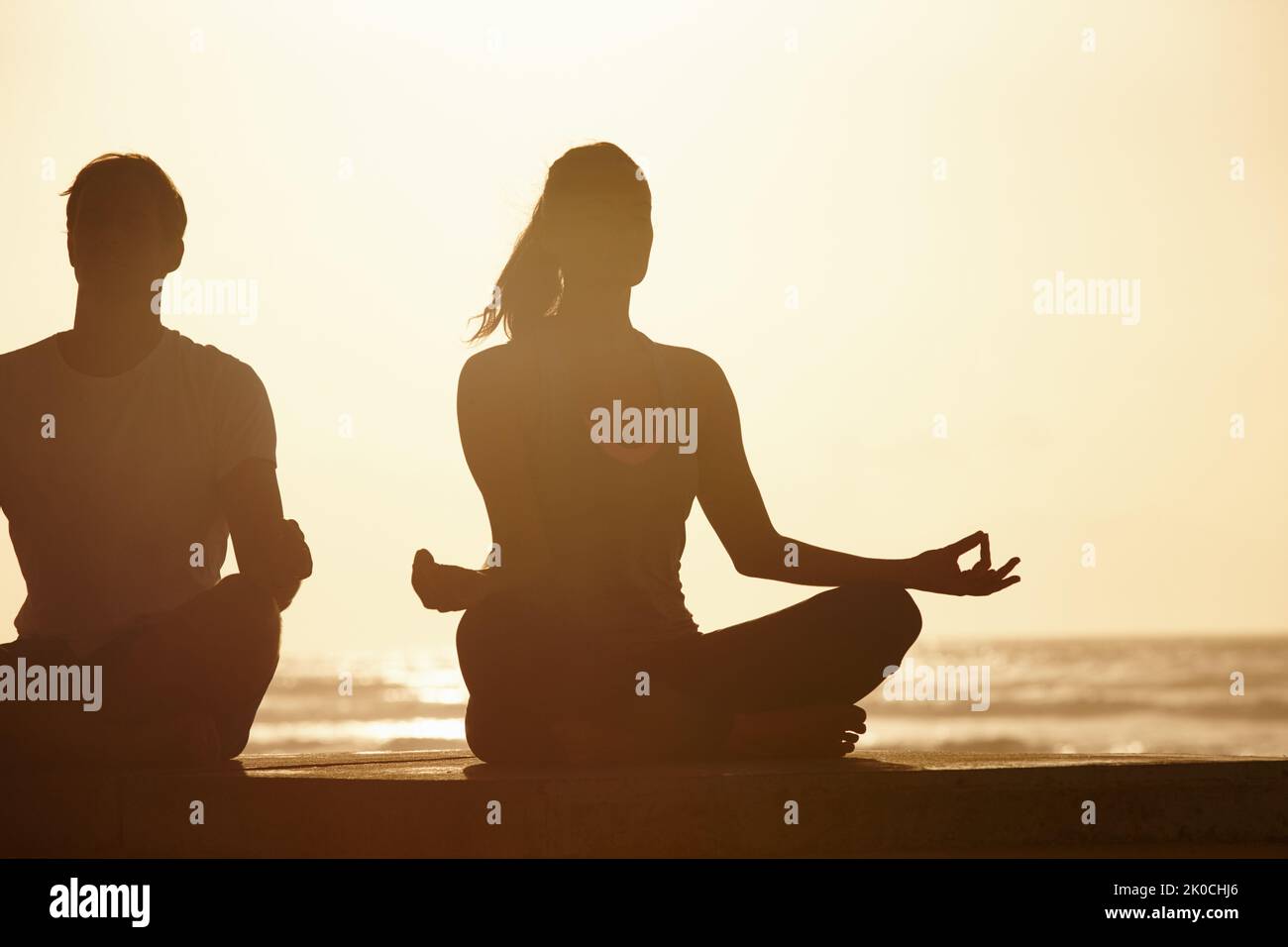 Der ideale Ort für Meditation. Ein Paar meditiert am Meer bei Sonnenuntergang. Stockfoto