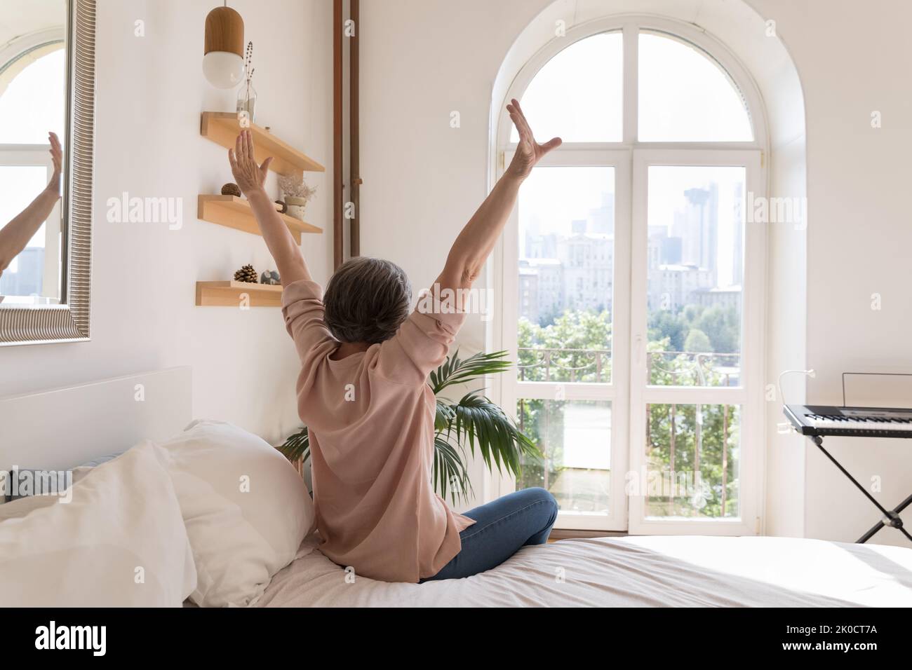 Entspannte ältere ältere Frau genießt es, im gemütlichen Schlafzimmer zu Hause zu sein Stockfoto