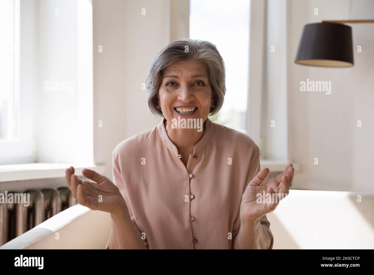 Glückliche, fröhliche ältere Dame, die von zu Hause aus einen Videoanruf entgegennahm Stockfoto