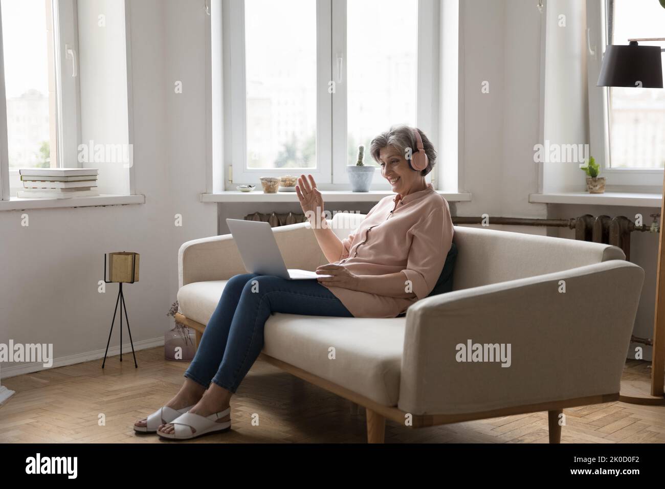 Fröhliche reife 60s-Mann-Frau in großen kabellosen Kopfhörern mit Laptop Stockfoto