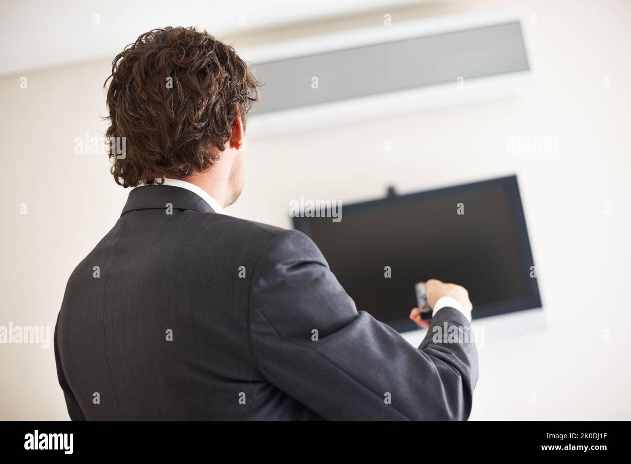 Geschäftsmann, der das Fernsehen anschalt. Rückansicht des Geschäftsmanns, der mit einer Fernbedienung den LCD-Fernseher anschalt. Stockfoto