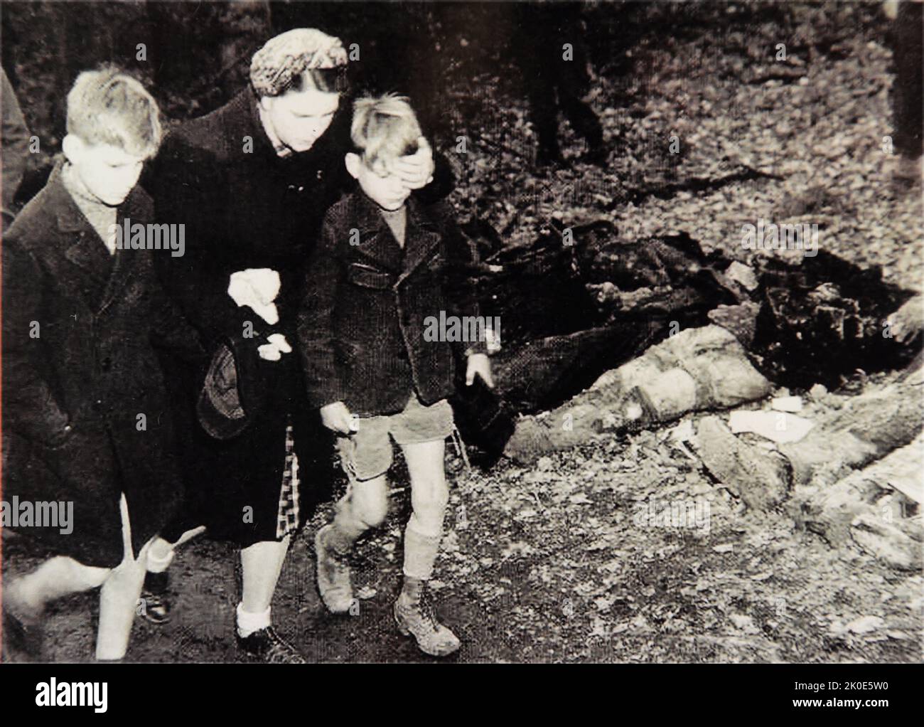 Die deutsche Mutter schützt die Augen ihres Sohnes, als sie an den Leichen von 57 Russen vorbeigeht, darunter Frauen und ein Baby, die aus einem Massengrab außerhalb der Stadt Suttrop exhumiert wurden. Die Opfer wurden gezwungen, ihr eigenes Grab zu graben und sechs Wochen vor der Ankunft amerikanischer Truppen von SS-Truppen geschossen. Stockfoto