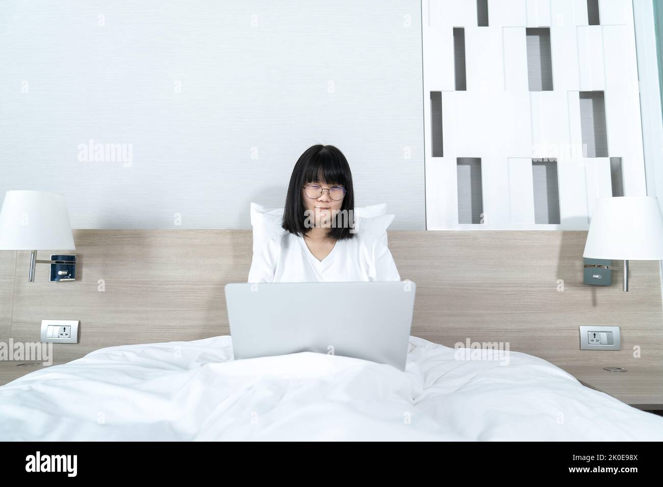 Brille Asian nette Frau arbeitet und spielt Laptop Notebook auf dem Bett in der Arbeit aus der Heimzeit. Stockfoto