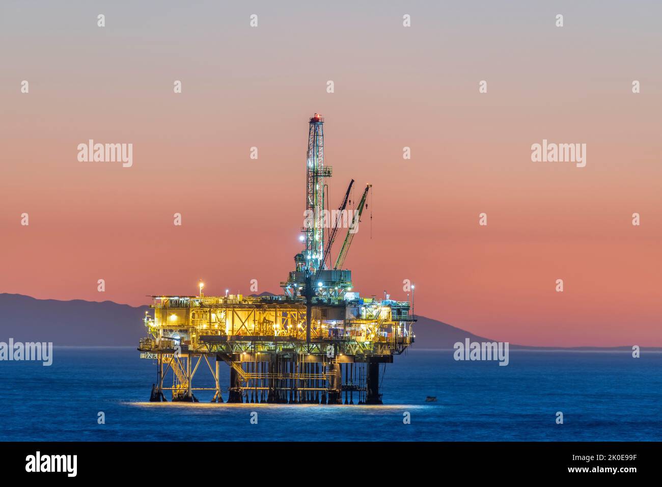 Dramatisches Bild einer Offshore-Ölplattform vor der Küste Kaliforniens vor einem rosafarbenen Winterhimmel, wenn die Sonne untergeht und die Lichter des Bohrgeräts leuchten. Stockfoto