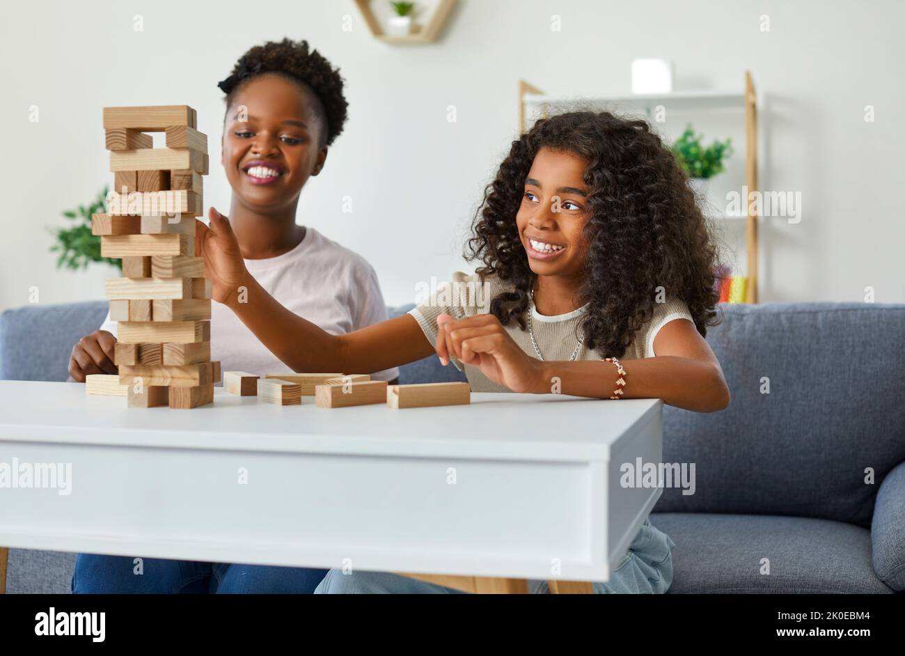 Happy Little African American Mädchen mit Mutter spielen Brettspiel sitzt auf dem Sofa in häuslicher Umgebung Stockfoto