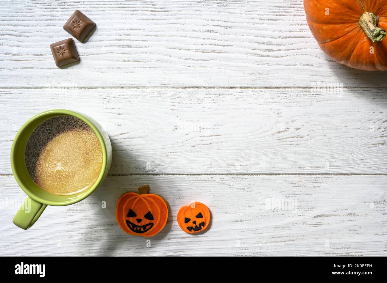 Halloween und Kaffee Thema, oranger Kürbis, Süßigkeiten und Tasse auf weißem Tisch, Draufsicht. Urlaub Essen auf Holzplanken Hintergrund mit Platz, flach legen. Teil Stockfoto