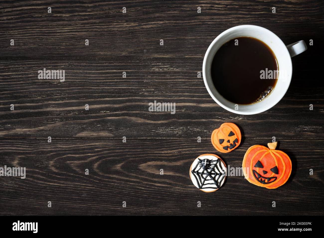 Halloween Hintergrund, Tasse Kaffee und Süßigkeiten auf Holztisch, Draufsicht. Orangefarbene Kürbis-förmige Kekse auf dunklen Holzplanken mit Platz. Party, Saison, Stockfoto