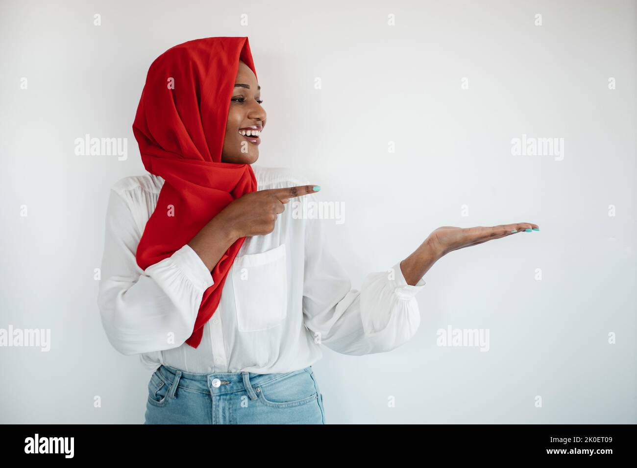 Überprüfen Sie dies. Glückliche afroamerikanische muslimische Frau im Hijab, die auf etwas in ihrer leeren Handfläche zeigt, Mockup Stockfoto