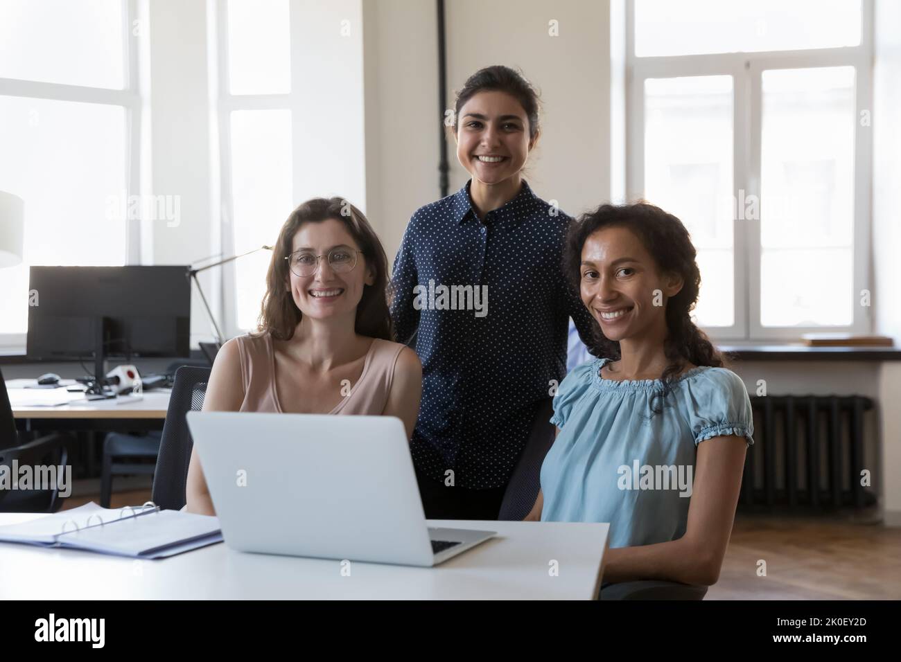 Glückliches, selbstbewusstes multiethnisches Geschäftsteam, das am Büroarbeitsplatz posiert Stockfoto