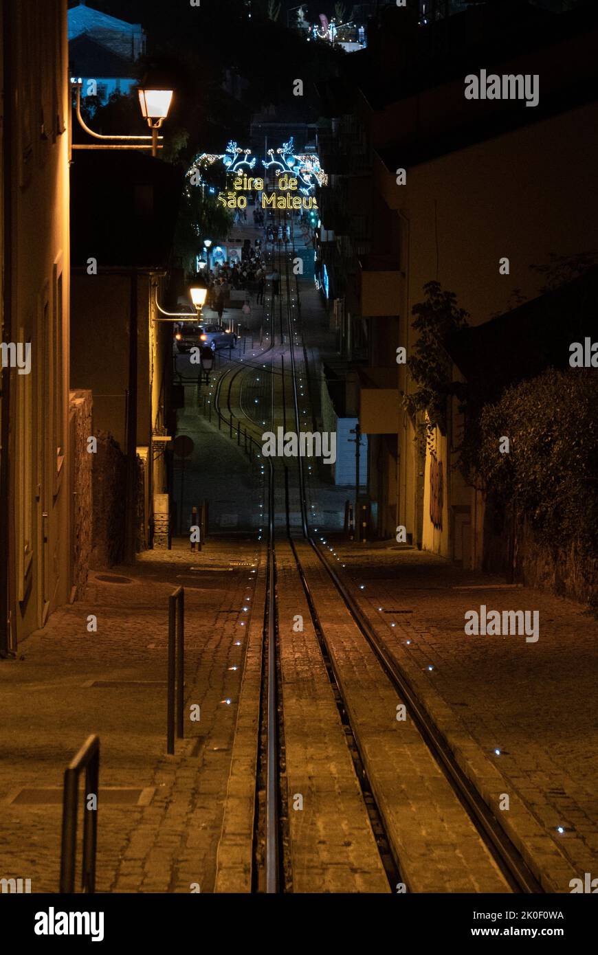 Nachtstraße mit einem steilen Hang und einer Straßenbahn- oder Eisenbahnstrecke, die zum Ende einer beleuchteten Dorfmesse führt Stockfoto