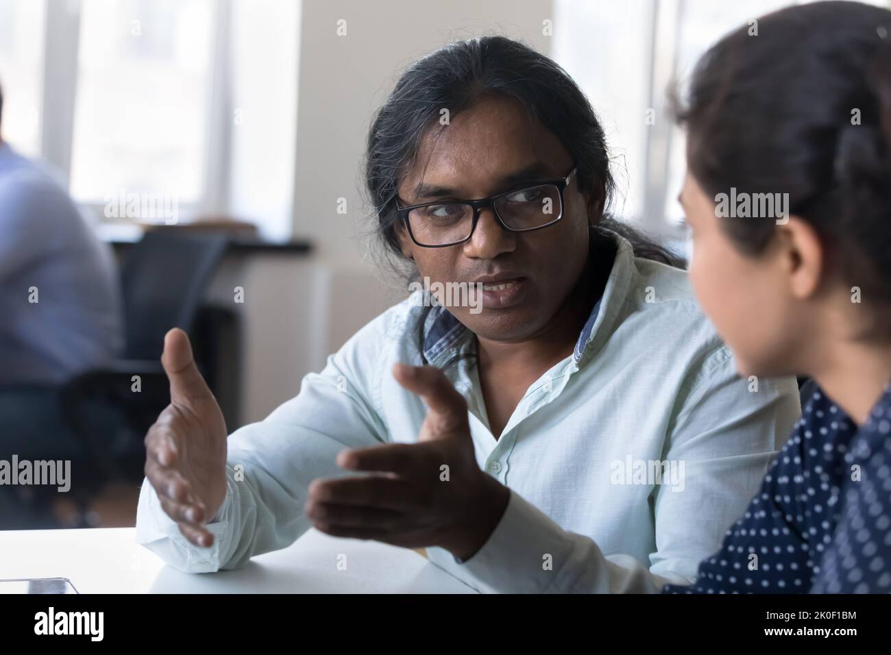 Männlicher indischer Mentor, der junge weibliche Praktikantin am Büroarbeitsplatz ausbilden wird Stockfoto