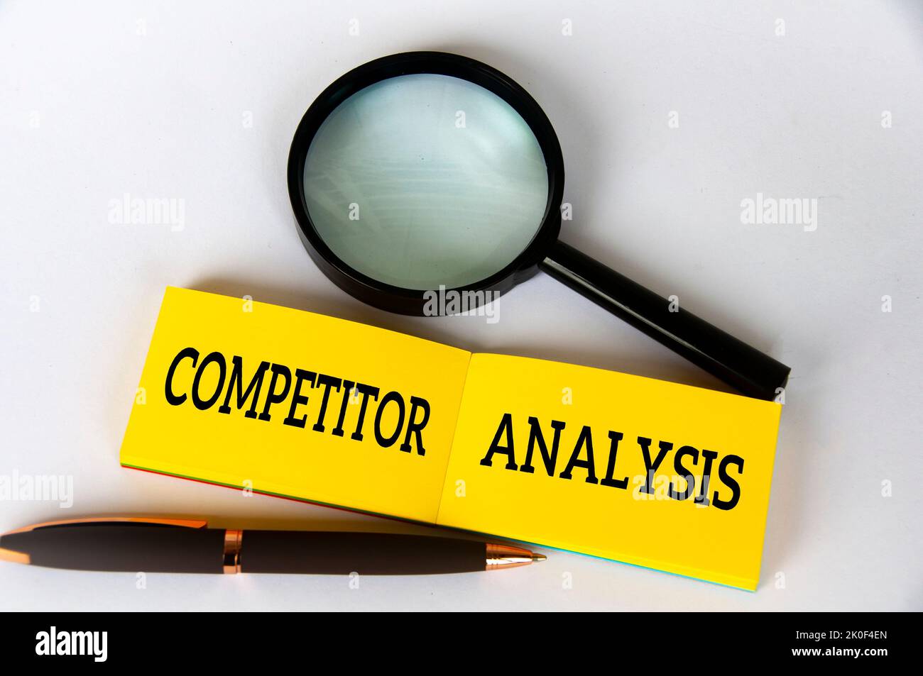 Konkurrenzanalyse-Text auf gelbem Notizblock mit Stift und Lupe auf weißem Hintergrund. Konzept zur Wettbewerbsanalyse Stockfoto