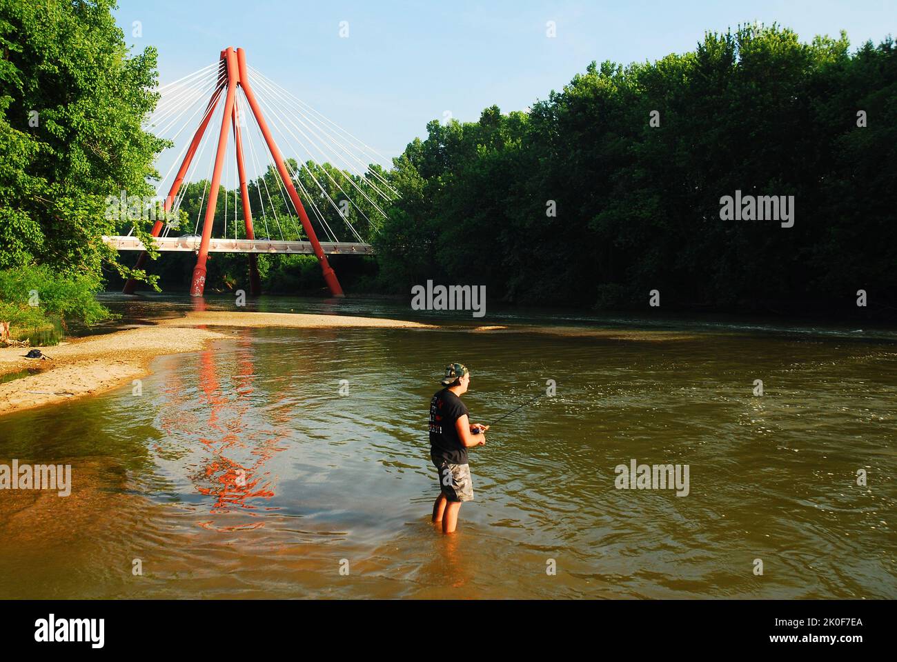 Ein erwachsener Mann fischt im White River mit der ultramodernen Second Avenue Bridge, die hinter ihm in Columbus Indiiana steht Stockfoto