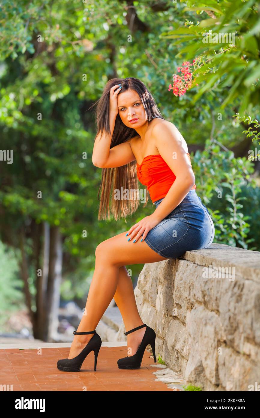 Teen Mädchen Denim Minirock Beine Fersen Blick auf Kamera verführt Hand berühren Haar posieren Stockfoto