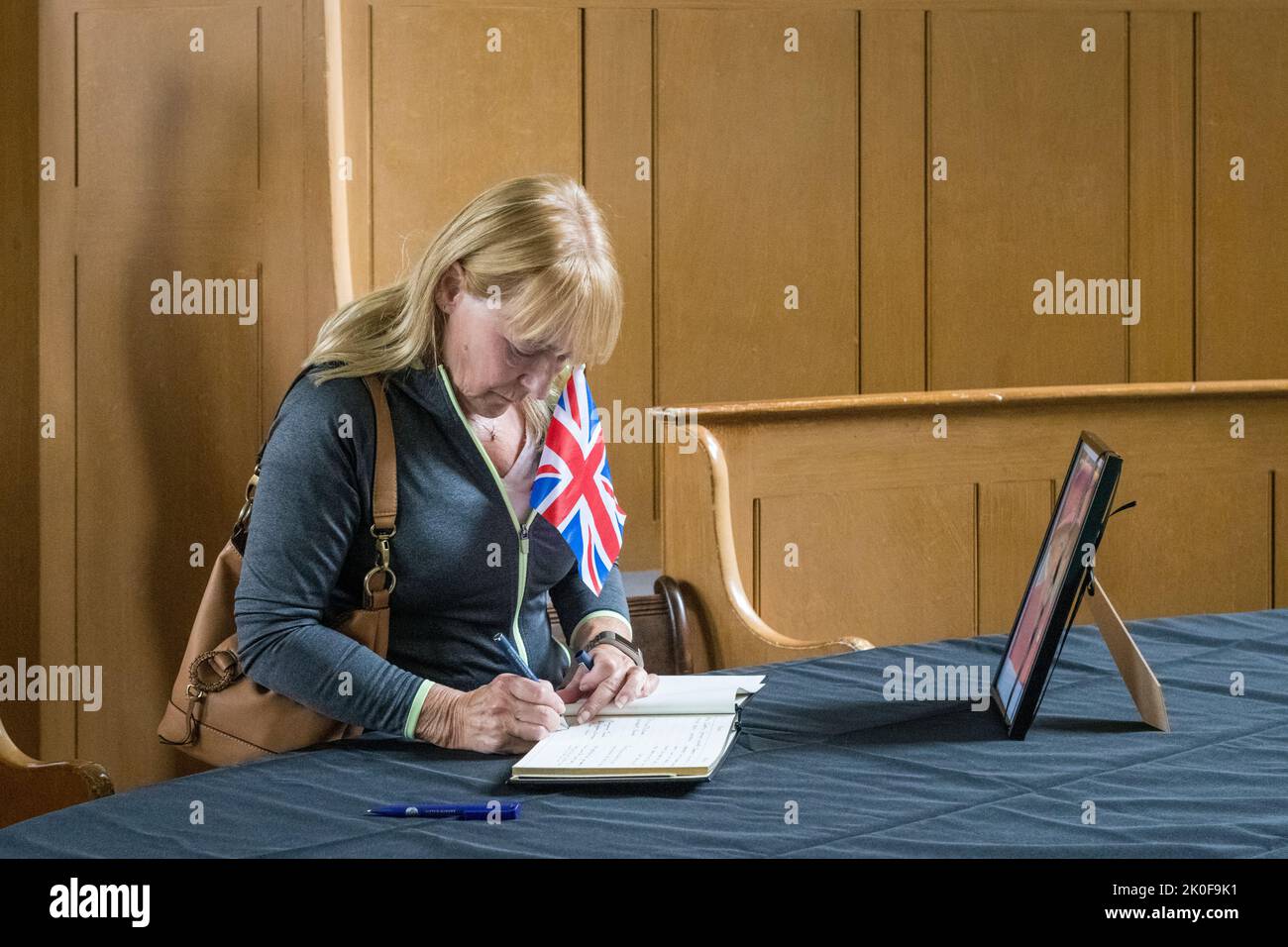 In der kleinen walisischen Grenzstadt Presteigne, der alten Grafschaftsstadt Radnorshire, unterschreibt eine Frau mit einem Union Jack ein Kondolenzbuch für die verstorbene Königin Elizabeth II. Das Buch wird im alten Gerichtssaal der Richterunterkunft in der Mitte der Stadt aufbewahrt. Stockfoto